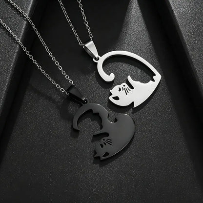 Two interlocking cat-shaped pendant necklaces on chains, one polished silver and one matte black, displayed on a textured black background.